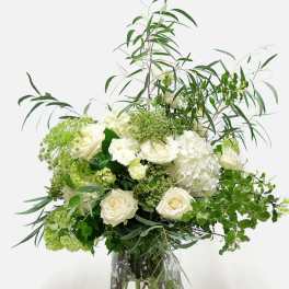 White roses and hydrangeas in a clear glass vase with airy greenery