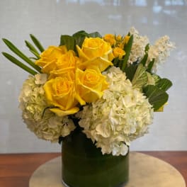 Yellow roses and white hydrangeas in a green glass vase