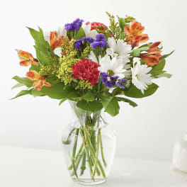 Mixed bouquet of daisies, carnations, and alstroemeria in a clear glass vase