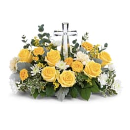 Yellow roses and white flowers arranged around a clear glass cross