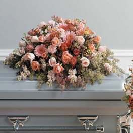Pastel floral spray on a casket with pink and peach blooms