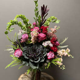Pink roses and dark cabbage in a glass vase with mixed greenery