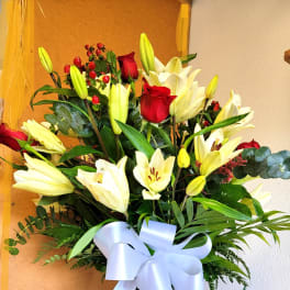 Tall bouquet of white lilies and red roses in a glass vase with a white ribbon