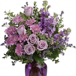 Lavender roses and purple mums arranged with filler flowers in a purple glass vase