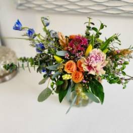 Mixed bouquet with orange roses, pink blooms, and blue flowers in a glass vase
