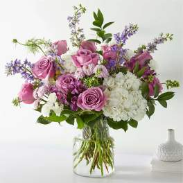 Pink and purple roses with white hydrangeas in a clear glass vase