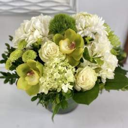 Compact arrangement of green orchids, white roses, hydrangeas, and mums in a round vase