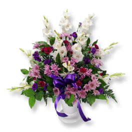 Bouquet of white, purple, and pink flowers in a white vase with a purple ribbon