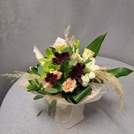 Bouquet of peach and white roses with dark purple flowers in cream wrap