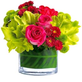 Pink roses and red flowers in a clear glass vase with bright green blooms