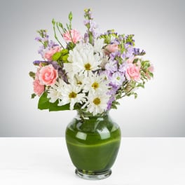 Mixed bouquet of white daisies, pink carnations, and lavender flowers in a green glass vase