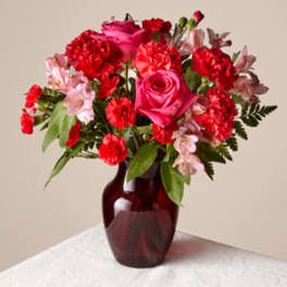 Red and pink flower arrangement in a dark glass vase