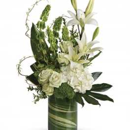 Tall white lilies, roses, and hydrangeas with green accents in a leaf-lined glass cylinder vase