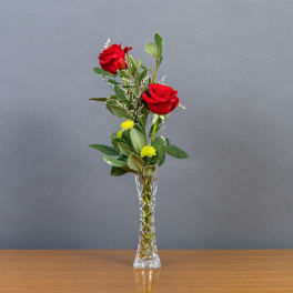 Two red roses in a clear glass vase with greenery