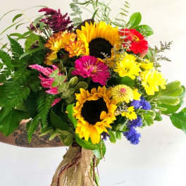 Hand-tied bouquet with bright yellow sunflowers, mixed colorful blooms, and burlap wrap