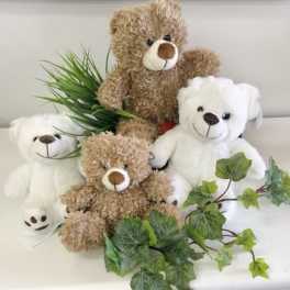 Three teddy bears with faux greenery on a white surface