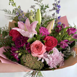 Hand-tied bouquet of pink lilies, roses, and mixed blooms wrapped in pink and kraft paper