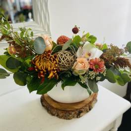 Low peach and rust flower arrangement with mums and orchid in a white bowl vase on a wood base