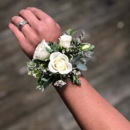 White rose wrist corsage with small white filler flowers worn on a wrist.