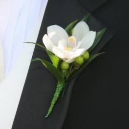 White orchid boutonniere with green berries pinned to a black suit lapel