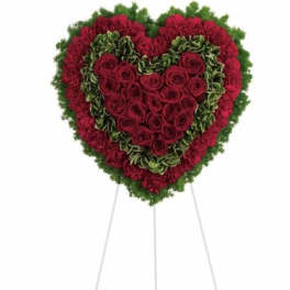 Heart-shaped standing floral arrangement of red roses and green flowers on a white easel
