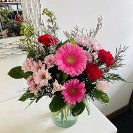 Mixed bouquet with pink gerbera daisies, red carnations, and pale pink blooms in a glass vase