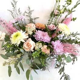 Loose pastel arrangement with pink mums, peach roses, and white blooms in a clear glass vase.