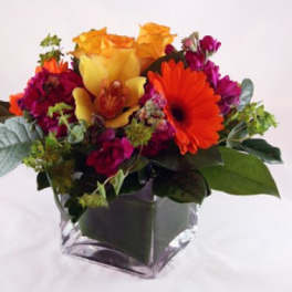 Colorful bouquet with orange and magenta flowers in a square glass vase