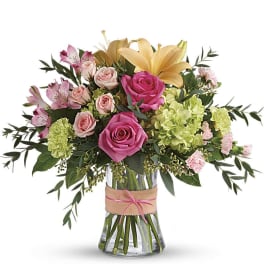 Mixed bouquet of pink roses, yellow lilies, and green hydrangeas in a clear glass vase