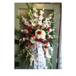 Tall standing floral spray with white flowers and red roses on a ribboned easel