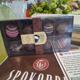 Box of assorted chocolate truffles on a counter with flower bouquets behind it