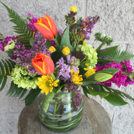 Colorful mixed bouquet in a glass vase with tulips, daisies, and purple blooms