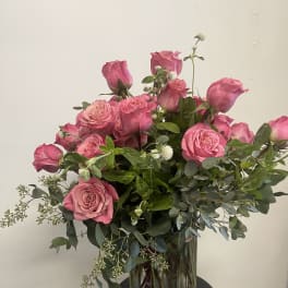 Pink roses arranged in a clear glass vase with greenery