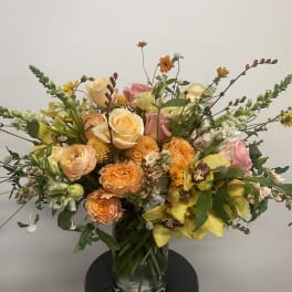 Large mixed bouquet of roses, orchids, and yellow blooms in a glass vase