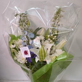 Wrapped bouquet of white, blue, and purple flowers with lilies and daisies