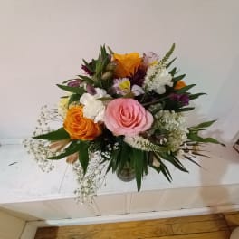 Mixed bouquet of pink and orange roses with white filler flowers in a glass vase