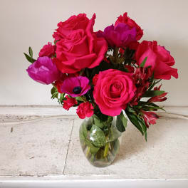 Pink and magenta roses with red accent flowers in a clear glass vase
