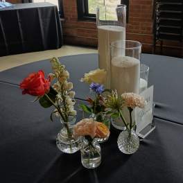 Small floral arrangements in glass vases around tall pillar candles on a table