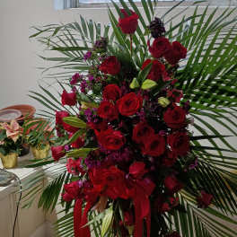 Tall arrangement of red roses with palm fronds and red ribbon
