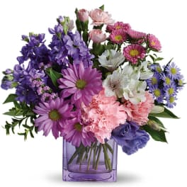 Mixed bouquet of purple daisies, pink carnations and white blooms in a lavender glass cube vase