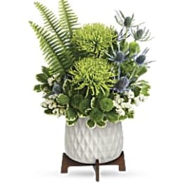Green floral arrangement in a white textured pot on a wooden stand