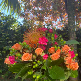 Orange and pink roses in a glass vase with green berries
