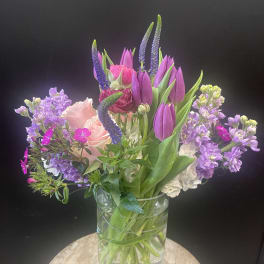 Mixed bouquet of purple tulips, pink roses, and lavender flowers in a glass vase