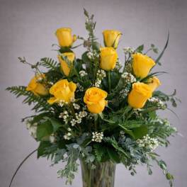 Yellow roses arranged in a clear glass vase with greenery
