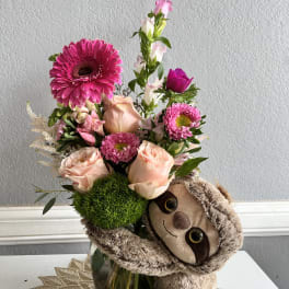 Pink flower arrangement with a plush sloth in a glass vase