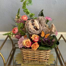 Basket arrangement with roses, mixed flowers, and a plush sloth
