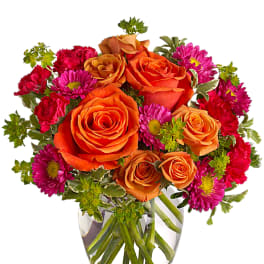Orange roses and pink daisies in a clear glass vase