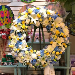 Large floral wreath with white lilies, blue hydrangeas, and yellow accents on an easel
