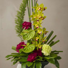 Tall floral arrangement with yellow orchids and magenta carnations in a black container