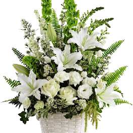 White lilies and roses arranged in a white basket with green accents